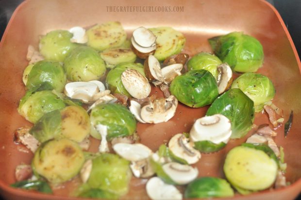 Sliced mushrooms and shallots are added to brussel sprouts and bacon in skillet.