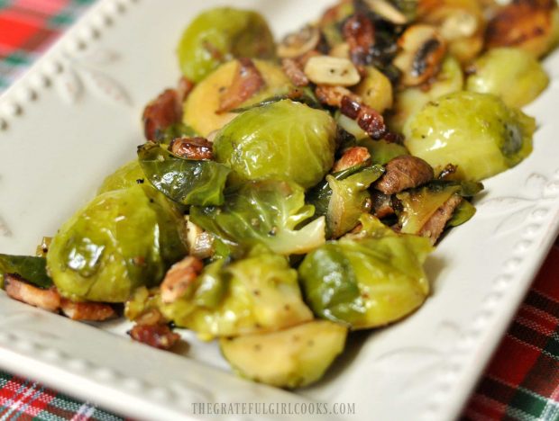 Cooked brussel sprouts on platter, with bacon and mushrooms.
