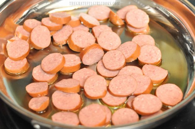 Smoked sausage slices are browned in a skillet.
