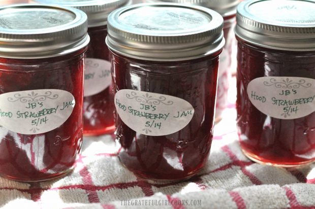 Jars of jam with labels, canned and cooling on dish towel