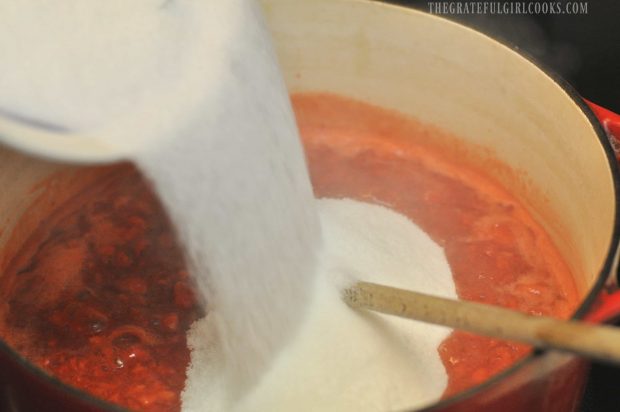Sugar being added to hot strawberry jam mixture in pan