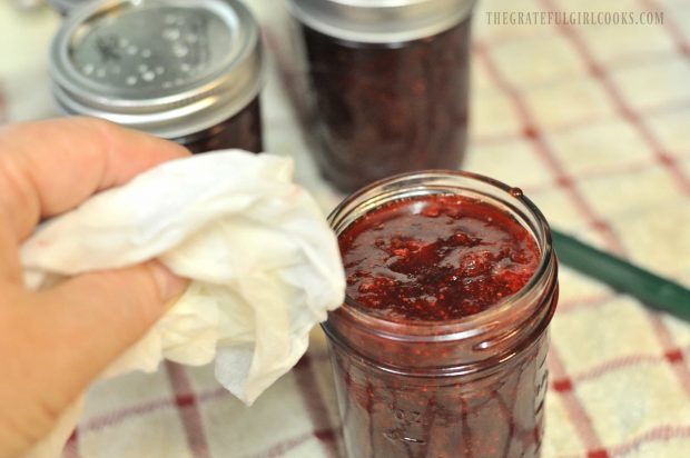 Wiping lid of canning jar filled with jam