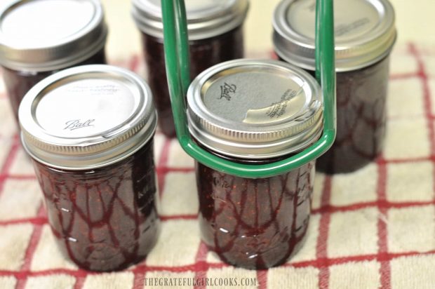 Jars of strawberry jam being placed on dish towel to cool