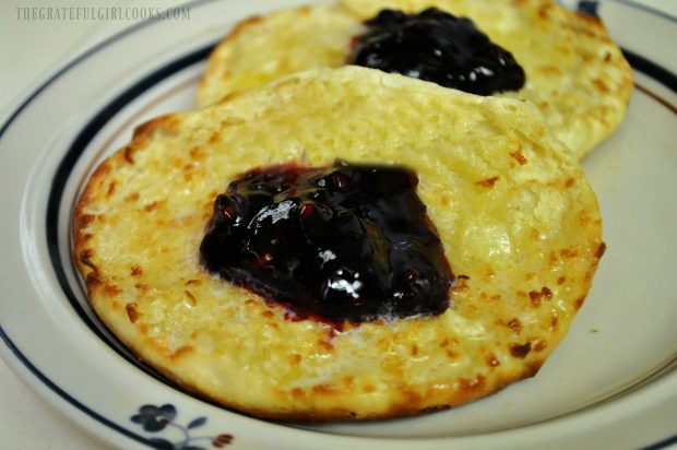 English muffins with butter and jam, on a small plate.