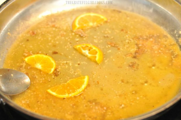 Orange juice, garlic and orange slices in skillet for citrus sauce to top pork cutlets.