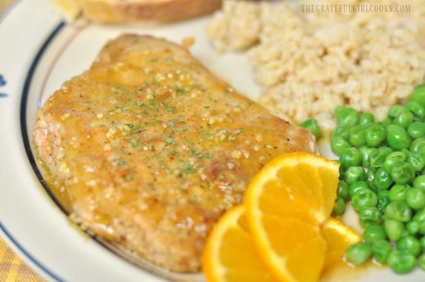 Cumin dusted pork cutlets on plate with rice, peas, and orange slices.