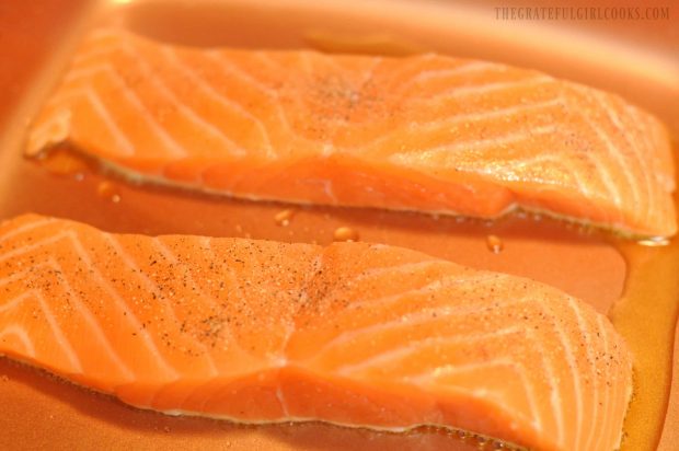 Two salmon fillets searing in copper skillet