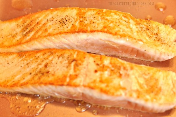 Two golden brown seared salmon fillets in skillet