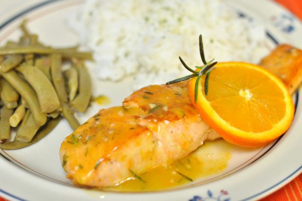 Orange rosemary glazed salmon, green beans and rice on a beige plate.