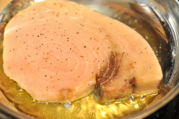 A swordfish fillet is being pan-seared in oil in a large skillet.