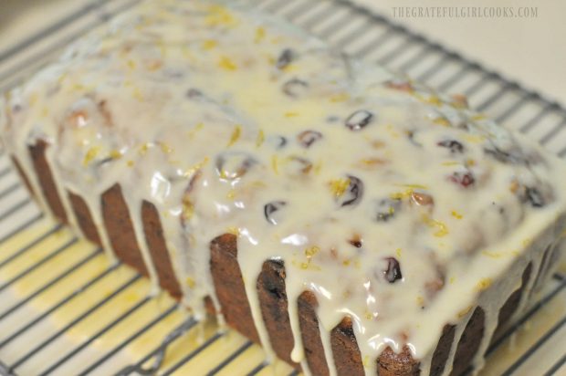 Cranberry orange loaf with orange icing on wire rack.