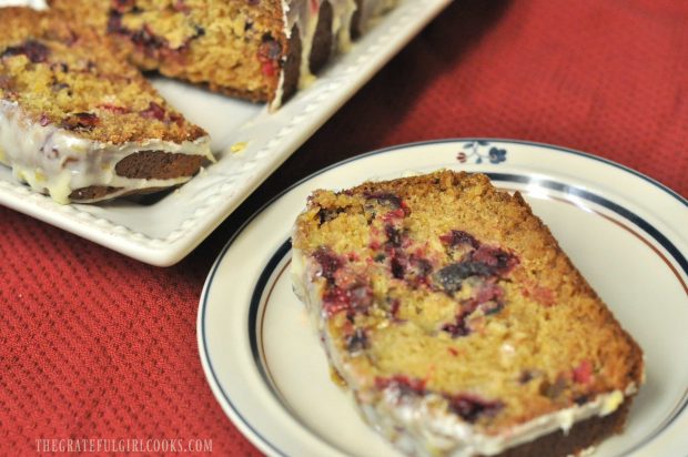 A slice of cranberry orange loaf with orange icing, on a plate.