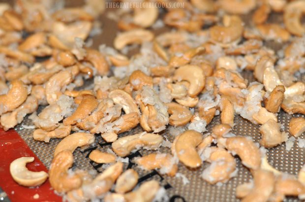 Coconut candied cashews sit on cooking mat while they cool down after baking.