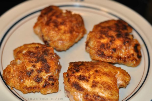 After browning in the skillet, chicken pieces rest on a plate.
