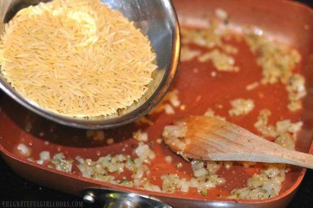 Uncooked orzo pasta is added to the cooked onions in skillet.