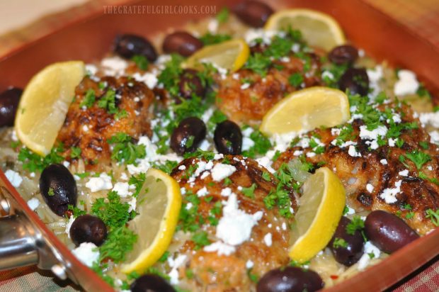 One Pan Greek Chicken And Orzo is served, garnished with kalamata olives, parsley and lemon slices.