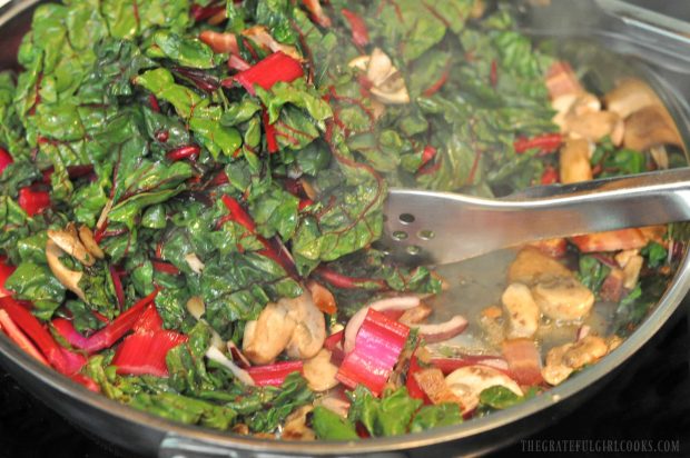 Swiss chard, bacon, red onion and mushrooms cooking in bacon drippings in skillet.