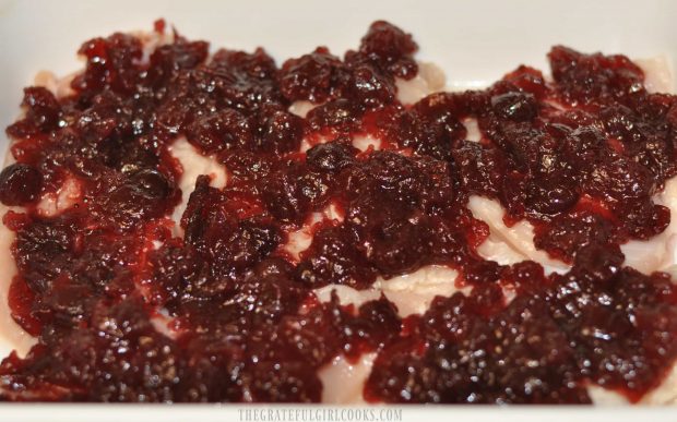 Whole cranberry sauce is spread over chicken breasts.