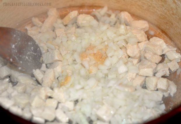 Minced garlic and chopped onions are added to the cooked chicken.