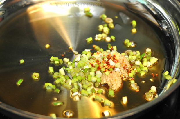 Green onions, garlic and red pepper flakes are cooked in a skillet with sesame oil.