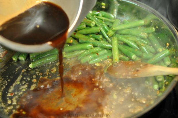Adding the Asian sauce to the spicy green beans in skillet.