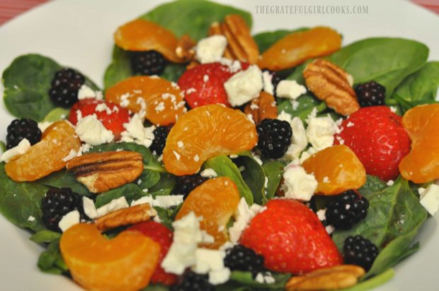 Berry orange spinach salad in a white bowl, ready for salad dressing.