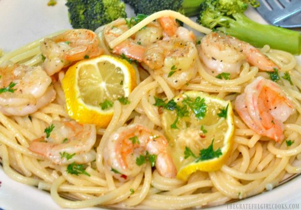 A portion of shrimp scampi is garnished with fresh parsley and lemon slices, to serve.