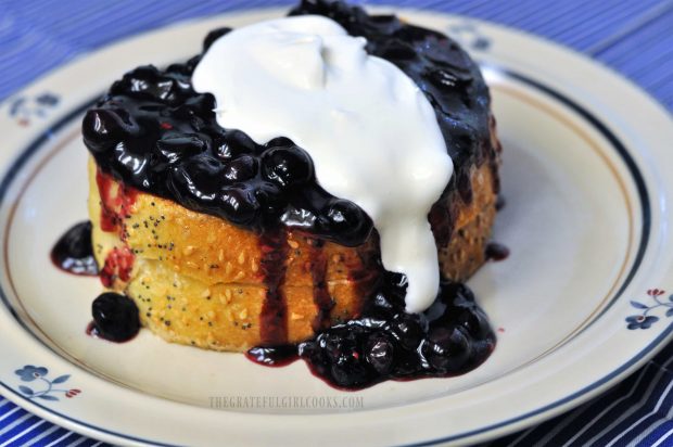 Blueberry and cream cheese stuffed french toast with whipped cream, on small plate