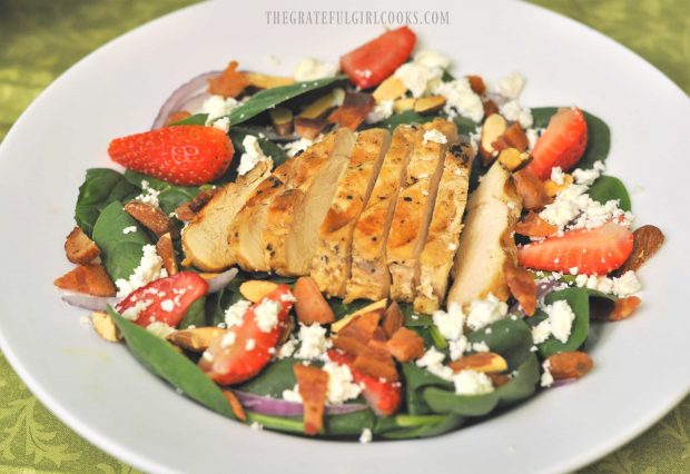 Chicken breast is sliced then served atop the spinach salad with avocado and strawberries.