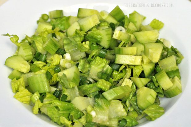 Diced romaine lettuce, green onions and cucumbers in white bowl.