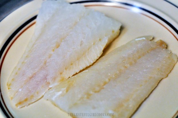 Pieces of cod on plate are patted dry before coating with sauce.