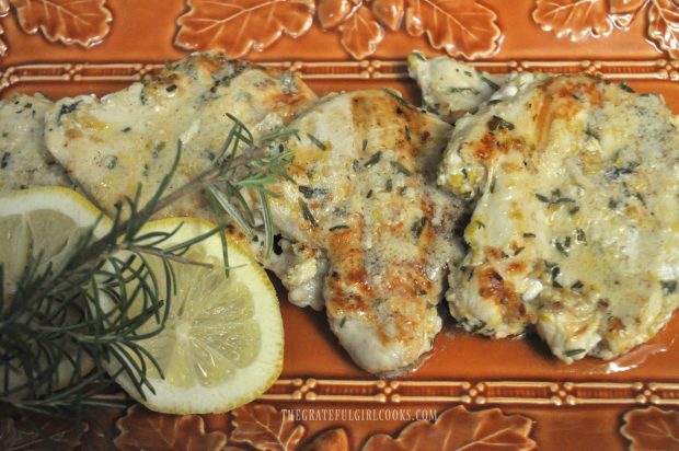 Lemon Rosemary Chicken Breasts are served on a platter garnished with lemon wedges and rosemary sprig.