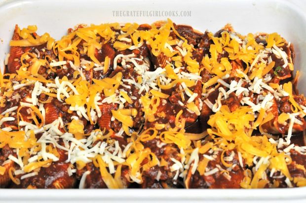 Mexican Stuffed Pasta Shells are covered with grated cheese before baking.