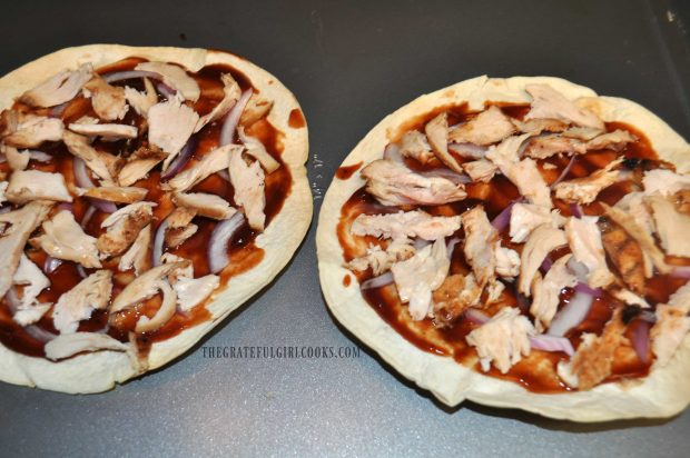 Cooked chicken pieces and red onion slices top the tortilla pizza.
