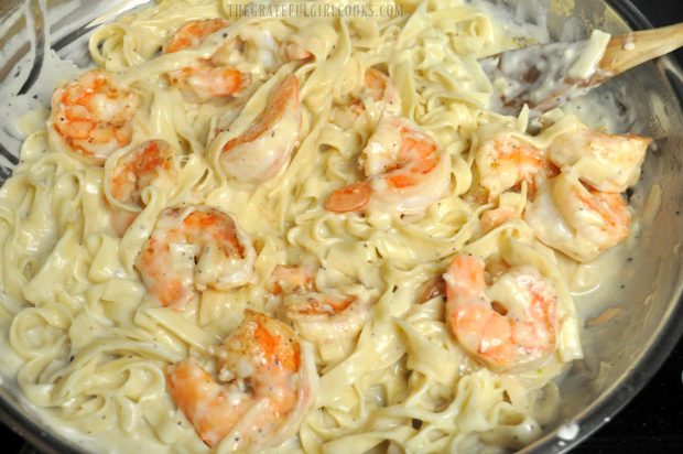 The pan-seared shrimp are added to the pasta and sauce in a skillet.