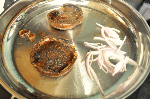 Marinated portobello mushrooms and some red onion slices are cooked for burgers.