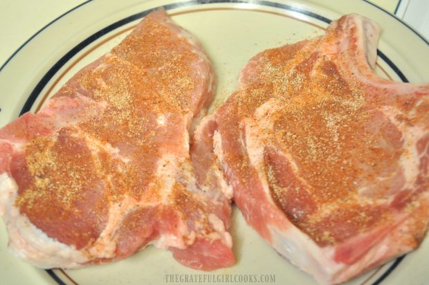 Bone in pork chops are seasoning with spices before pan-searing.