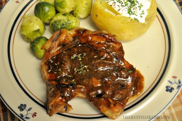 Smothered pork chops on plate with baked potato and brussel sprouts on the side.