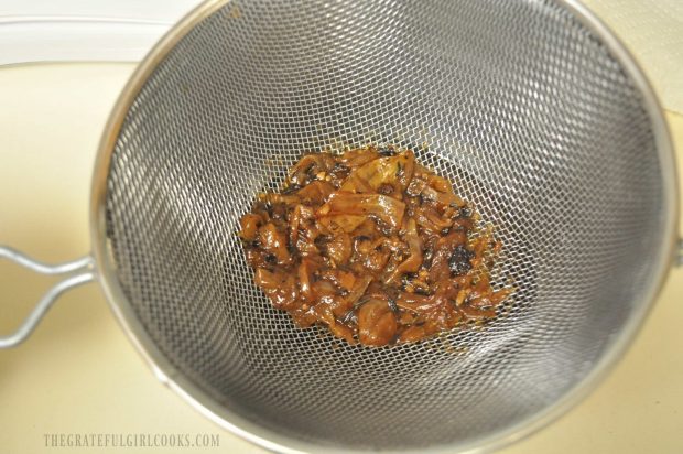 Cooked onions are strained with sauce going into a bowl underneath strainer.