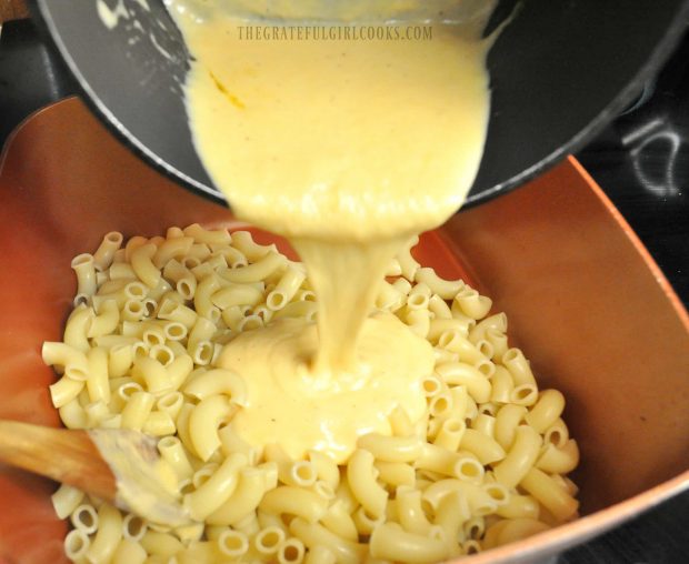 Cheese sauce is poured over hot macaroni in pan.