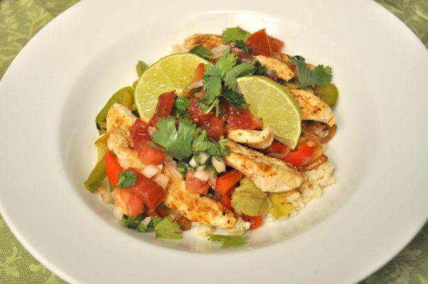 The chicken fajita rice bowl is served in a white bowl, with a lime and cilantro garnish.