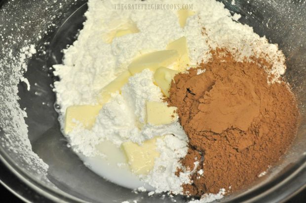 Powdered sugar, butter, cocoa powder and milk, in bowl before placing in microwave to make fudge.