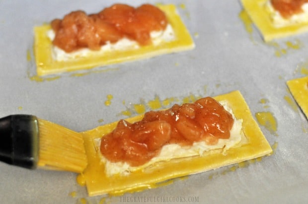 Egg yolk is brushed onto edges of apple cream cheese pastries before baking.