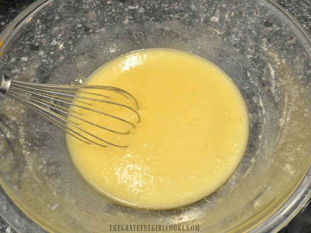 Yellow muffin batter in clear mixing bowl with whisk