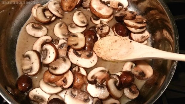 Mushrooms and wine cooking in metal skillet with a wooden spoon