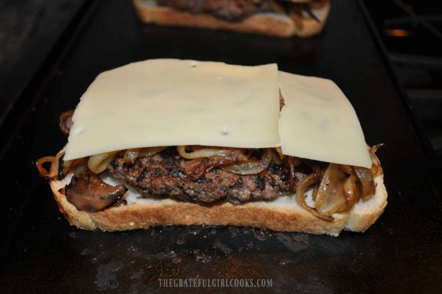 Swiss cheese slices are placed on top of onions on patty melt.