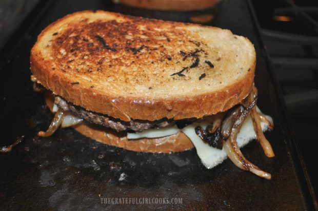 Grilled Patty Melt is flipped over to cook other side of bread on grill until golden brown.