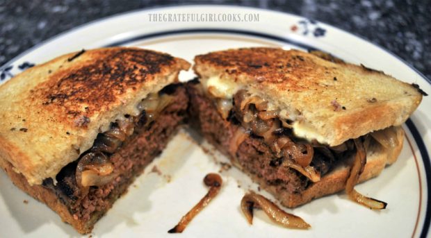 Grilled patty melt is cut in half on a plate.