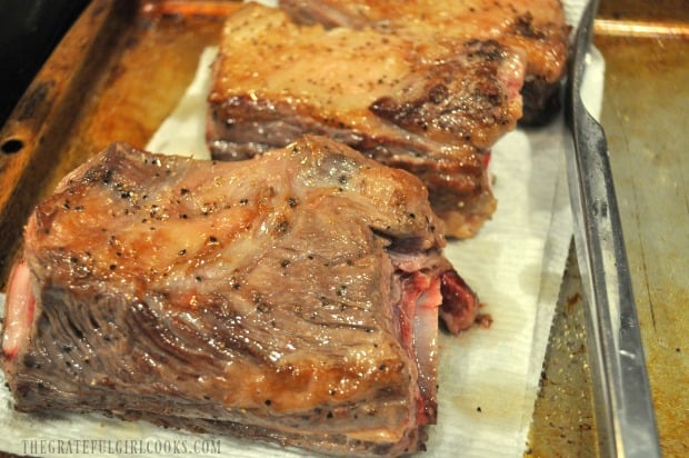 Browned meat resting on paper towels on baking sheet