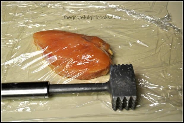 Chicken covered in plastic wrap, with meat mallet 